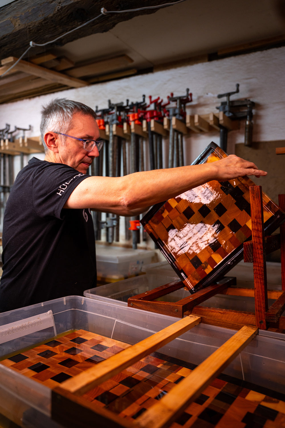 Man inspecting a varnished wooden board with a checkerboard pattern in a carpentry workshop.